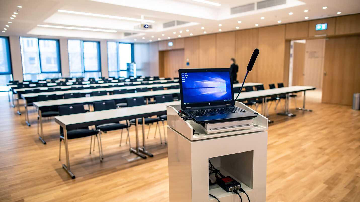 IT-Technik auf Rednerpult vor parlamentarischer Bestuhlung