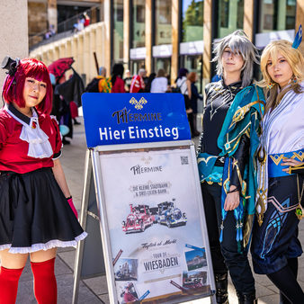 Drei Frauen in Manga-Kostümen stehen vor der THermin Haltestelle