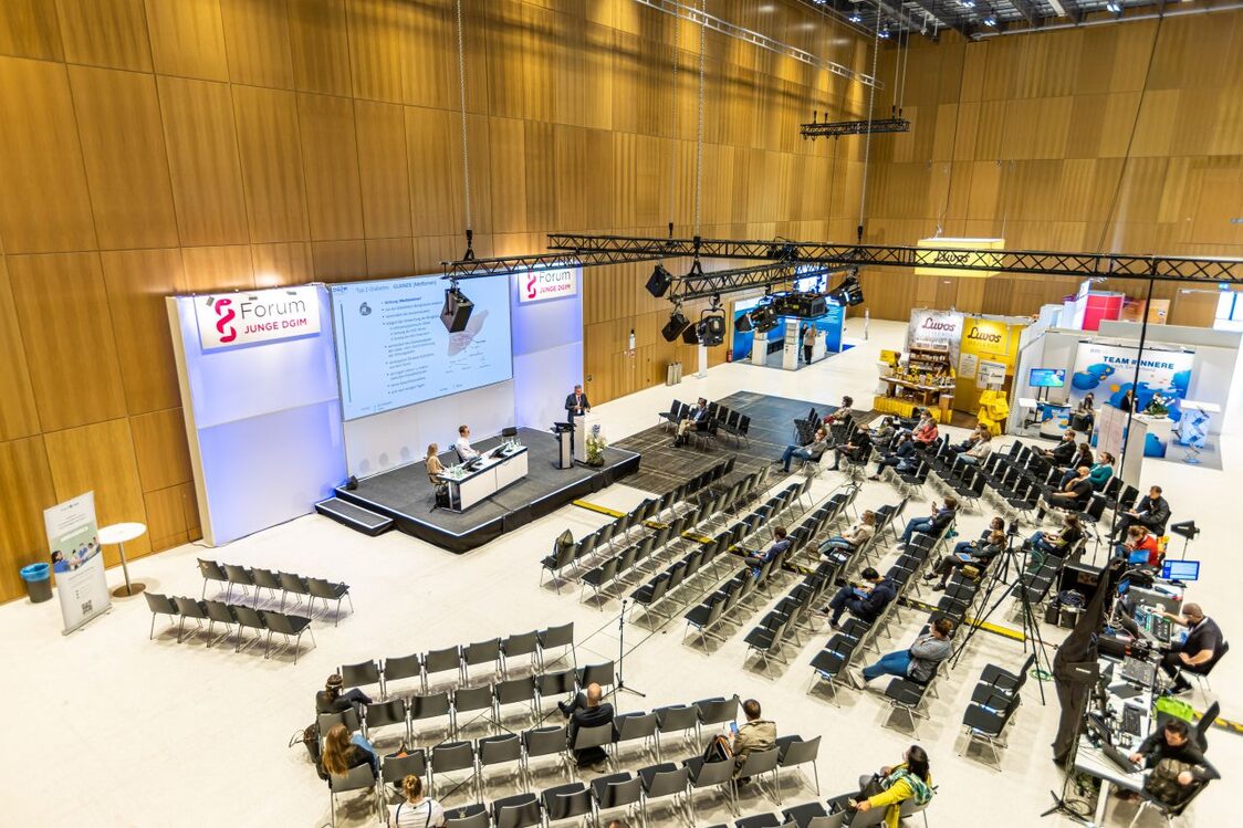 Veranstaltungsgäste in der Messehalle sitzen und hören den Vortrag zu