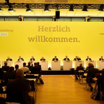 Gäste sitzen vor der gelben Bühne mit 11 Rednern