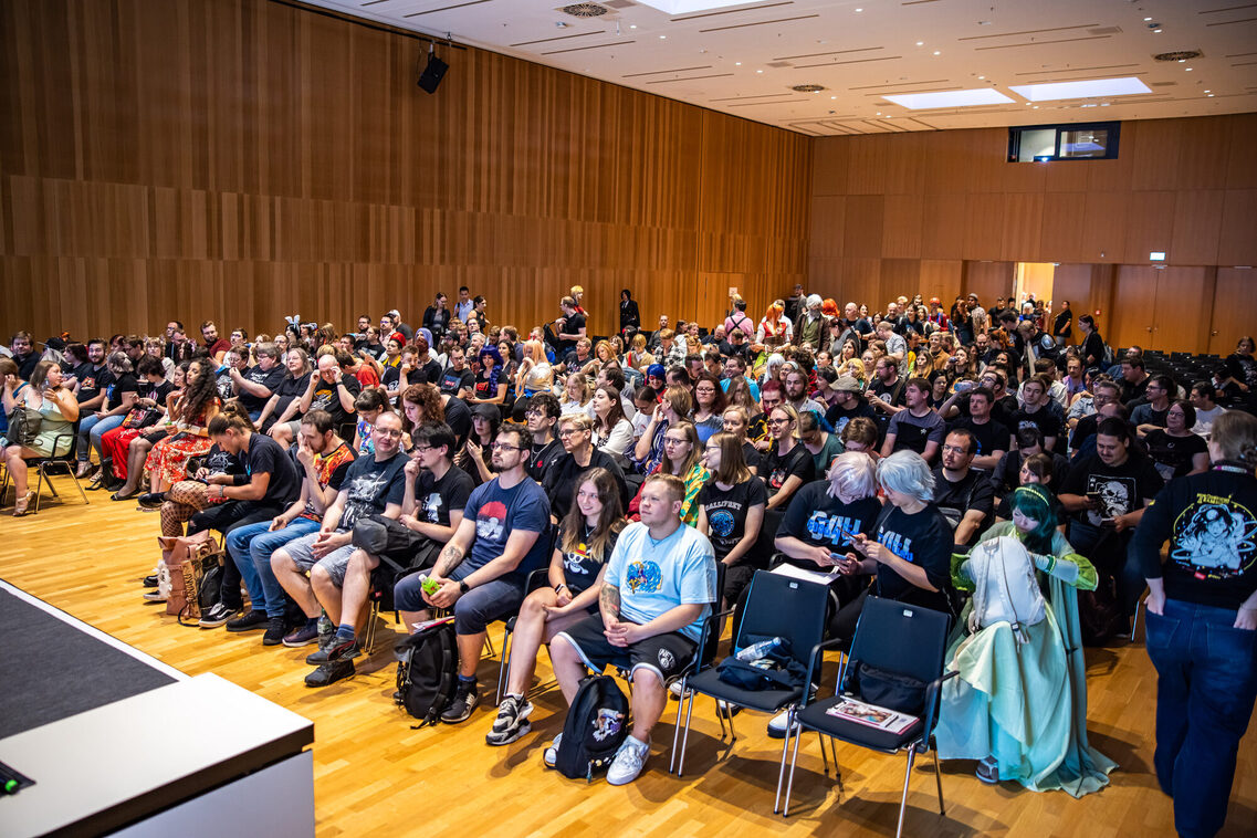 Gäste sitzen in der Reihenbestuhlung und hören den Vortrag zu