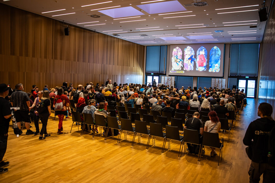 Gäste sitzen in der Reihenbestuhlung und hören den Vortrag zu
