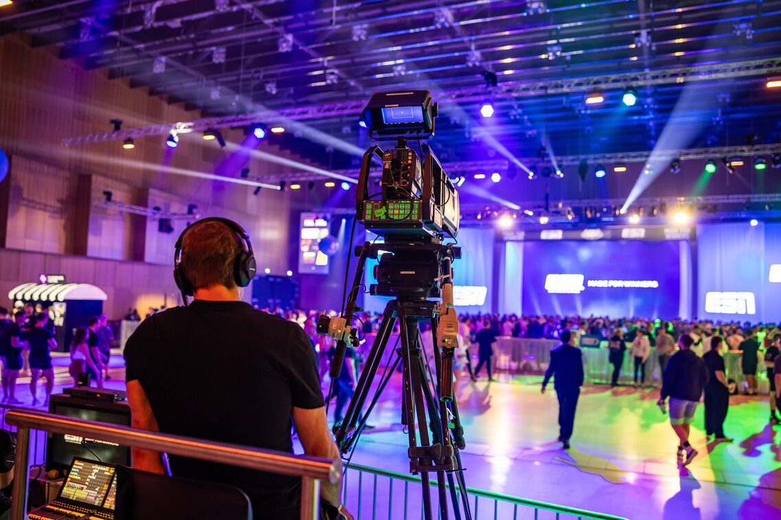 Ein Mann steht hinter der Kamera in der beleuchteten Messehalle