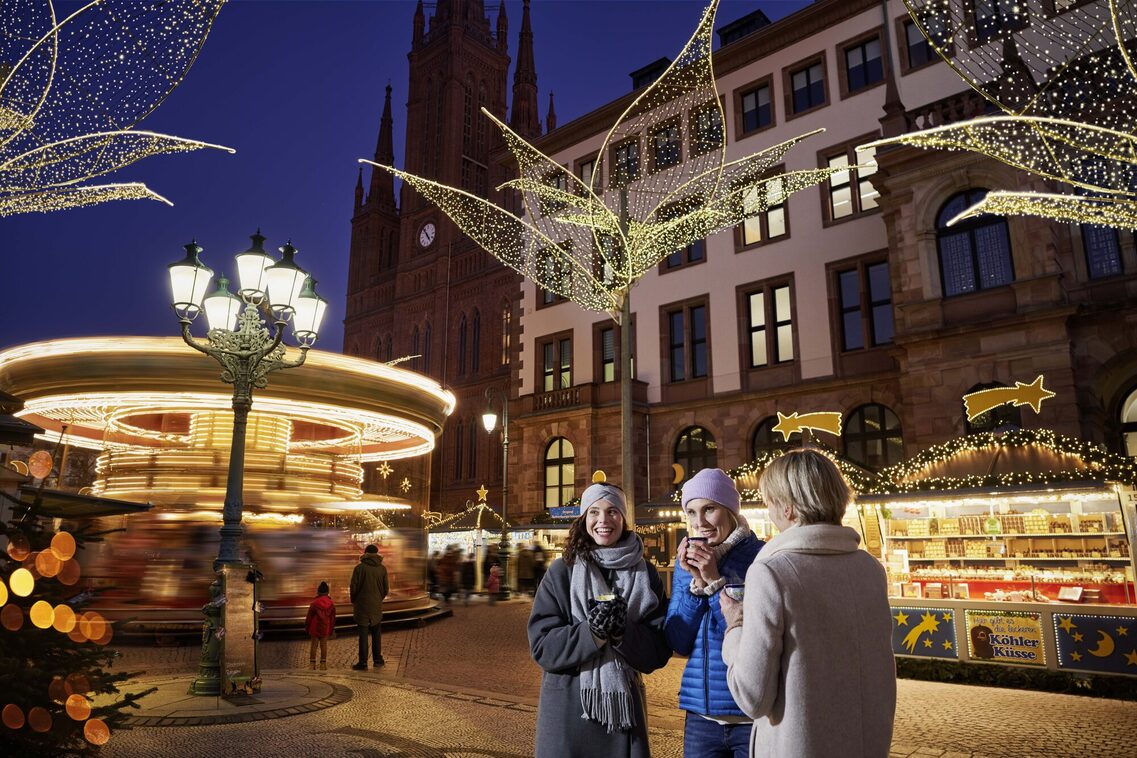 Drei Frauen trinken ein warmes Getränk auf dem Weihnachtsmarkt