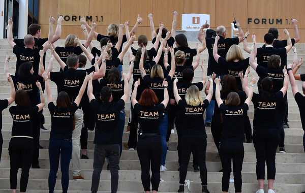 Gruppenfoto des Teams von hinten. Personen stehen auf Stufen und strecken die Fäuste gen Himmel.