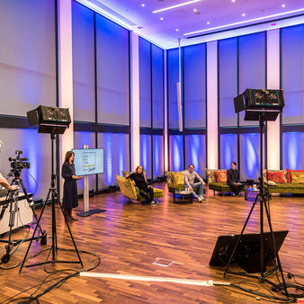 Eine Moderatorin, drei Referenten und ein technischer Mitarbeiter bereiten sich im Studio für Live-Stream vor